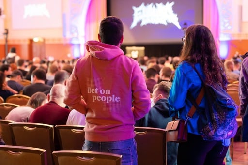 A man and a woman from the back. The man is wearing a pink hoodie with ‘Bet on people’ printed on it.