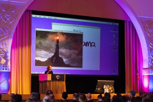 Mel Kaulfuss presenting. Her presentation is on the screen behind her and looks like an old version of Mac OS.